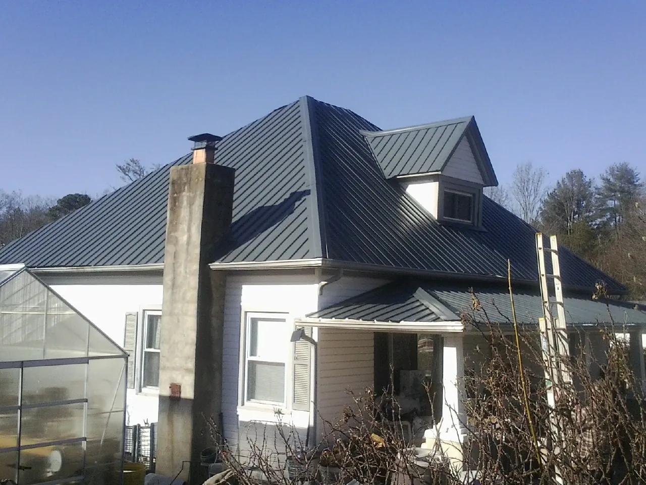 Dark blue standing seam metal roof on a white farmhouse with dormer — Slate & Tile Roof Repair by Roofing Brothers in Maupin