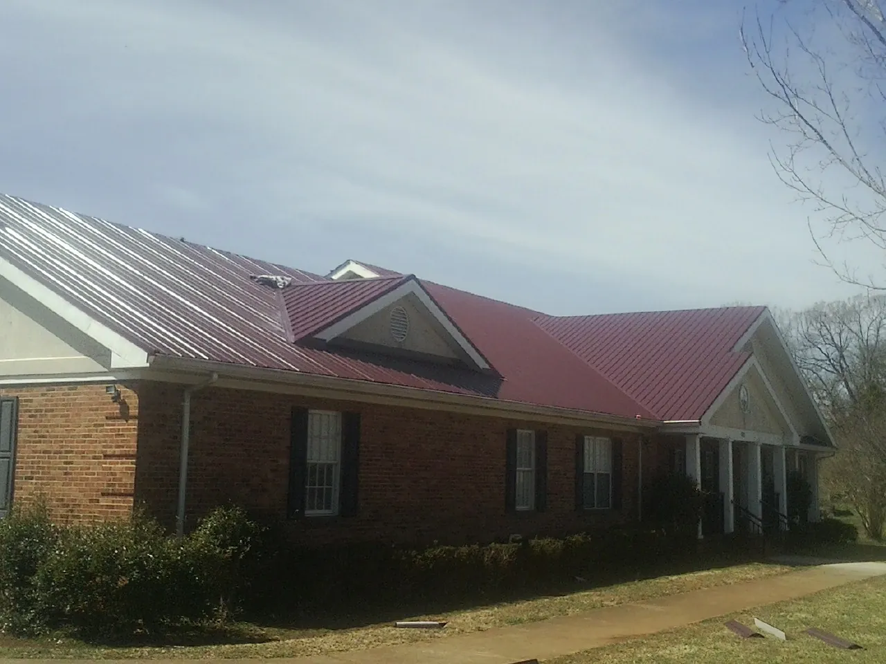 Red metal roof with gabled entries on a long brick building, from a Hail Damage Roof Repair job in Maupin