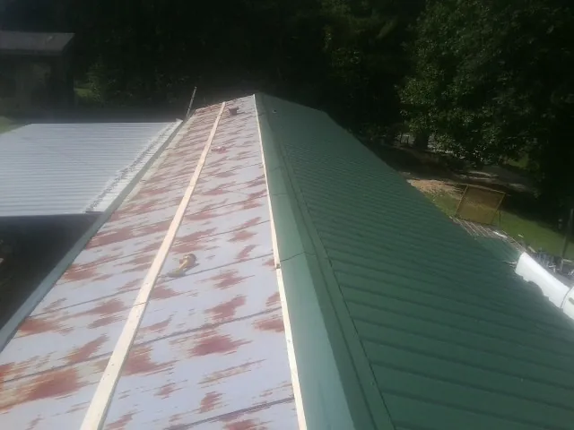 Old rusted panels beside newly installed green metal roofing — Wind Damage Roof Repair by Roofing Brothers in Maupin