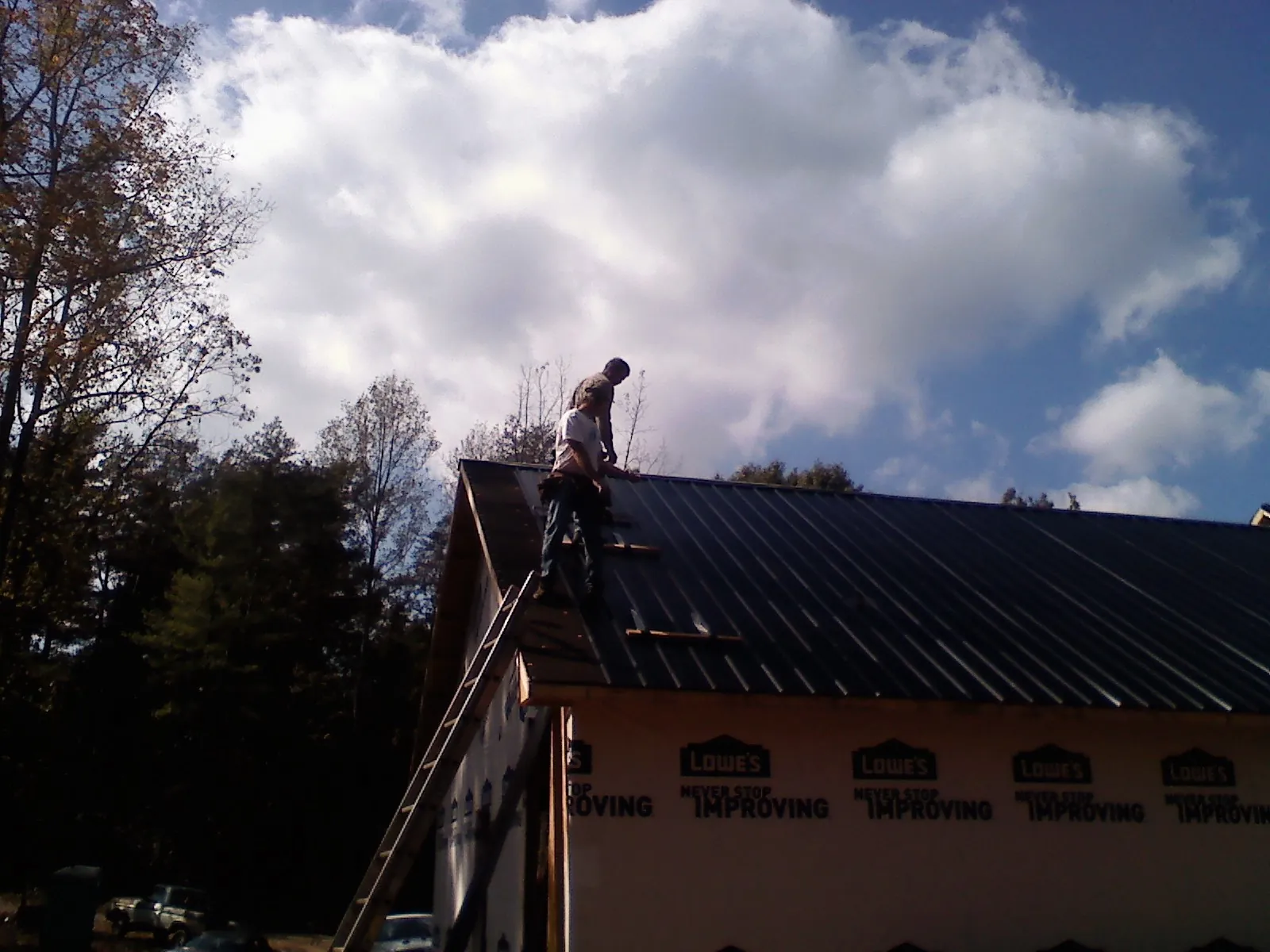 Roofer fastening dark metal panels high against a cloudy sky, from a Roof Inspection job in Maupin