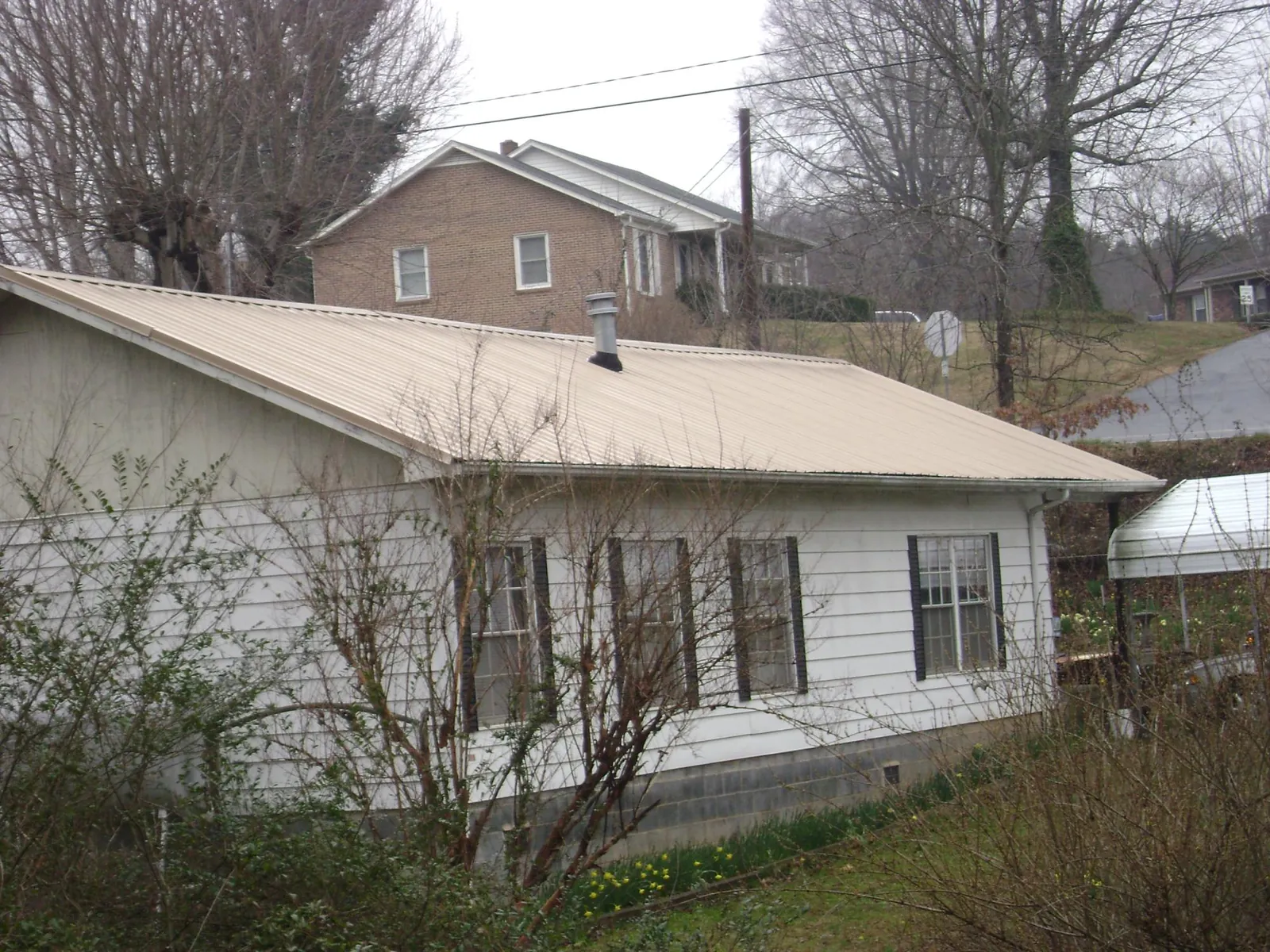 Tan metal roof on a white sided house set into a hillside — Commercial Roofing by Roofing Brothers in Maupin