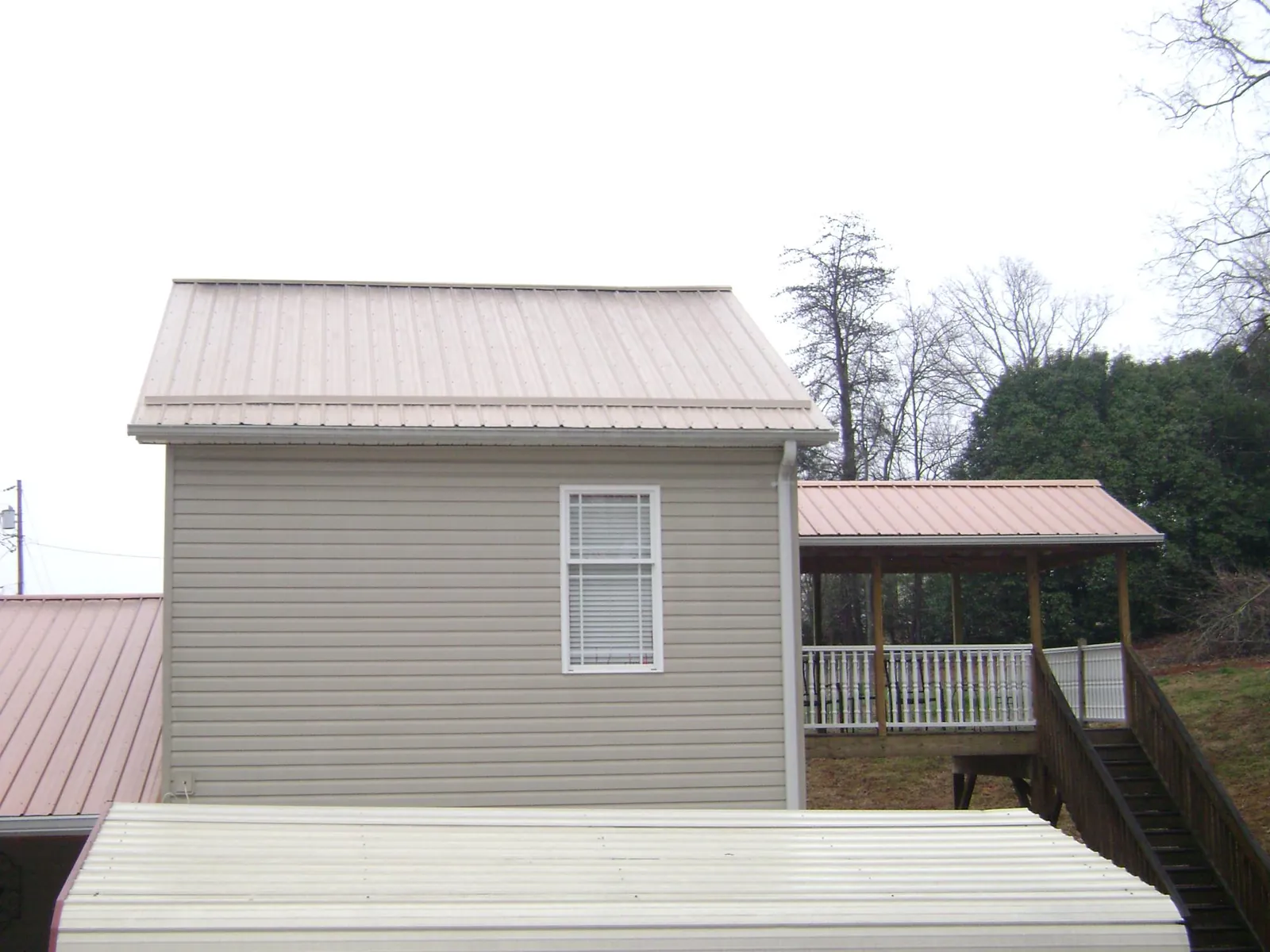Tan metal roofs on a two story addition and attached porch, from a Roof Replacement job in Maupin
